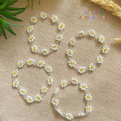 three bracelets with yellow and white flowers on them sitting next to some wheat stalks