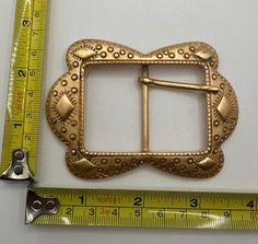 a gold belt buckle sitting next to a measuring tape