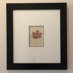 a black frame with a red maple leaf on the front and bottom, hanging on a wall