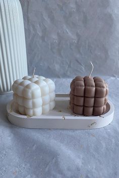 two candles are sitting on a tray next to a white vase and another candle holder