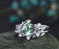 a green and white ring sitting on top of a rock with leaves around it's edges