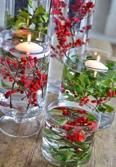 three glass vases filled with red berries and greenery on top of a wooden table