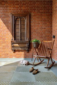 a wooden rocking chair sitting in front of a brick wall next to a planter