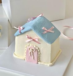 a cake shaped like a house with pink and blue decorations on the roof, sitting on top of a white box