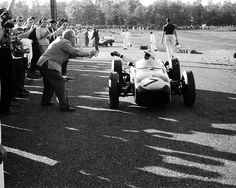 an old photo of a man driving a race car in front of a group of people