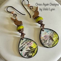 a pair of earrings with bird and flower designs hanging from it's hooks on a white plate