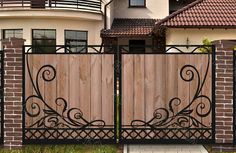 a wooden gate with wrought iron designs in front of a house