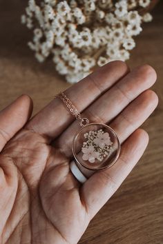 a hand holding a tiny necklace with flowers in it