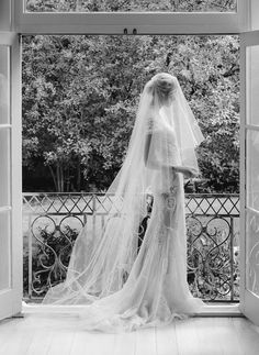 a woman in a wedding dress is looking out an open door at the trees outside