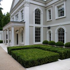 a large white house with hedges in the front yard