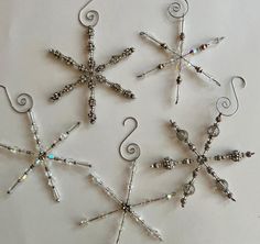 four snowflakes made out of glass beads and silver wire on a white surface