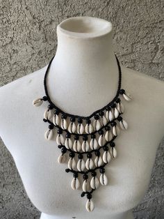 Vintage Cowrie Shell necklace , Afrocentric Jewelry Features rows of cowrie shells on a black braided cord Cowrie Shells symbolize prosperity and destiny. In  some West African cultures they are also a sign of fertility. In ancient times cowrie shells were also used as currency in some cultures.  Length: 12 inches Width: approximately 8 inches Handmade Please note that this is a vintage item. Vintage items show signs of age, wear and in some instances chips or missing pieces which add to their charm as preloved items. Please review photos Thanks Black Artisan Necklaces For Beach, Black Artisan Necklace For Beach, Artisan Black Necklace For Beach, Artisan Black Jewelry For The Beach, Traditional Cowrie Shell Jewelry For Beach, Handwoven Black Jewelry For The Beach, Black Handwoven Jewelry For Beach, Black Handwoven Jewelry For The Beach, Bohemian Black Beads Jewelry