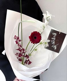 a woman holding a bouquet of white and red flowers in her hands with a card