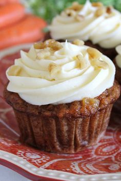 three cupcakes with white frosting and walnuts on a red floral plate