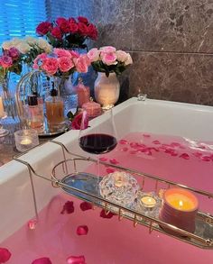 a bathtub with rose petals floating in the water next to candles and vases