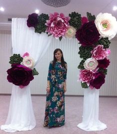 a woman standing in front of an arch made out of flowers and white drapes