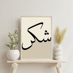 an arabic calligraphy is displayed on a shelf next to a vase with some flowers