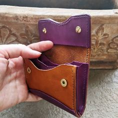 a hand holding a purple and tan leather wallet with two buttons on the front pocket