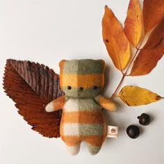 a small stuffed animal sitting next to leaves and berries on a white surface with autumn colors