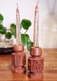 two wooden candlesticks sitting on top of a table next to a potted plant