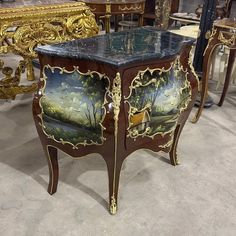 an ornately painted side table with gold trimmings and black marble top, surrounded by other antique furniture