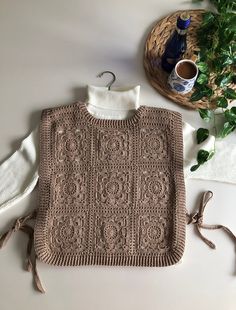 a crocheted sweater sits on top of a table next to a potted plant