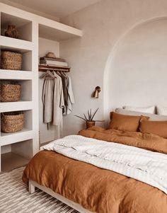 a bed with an orange comforter in a bedroom next to a white wall and shelves