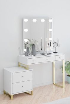 a white dressing table with two drawers and a mirror on it, next to a potted plant