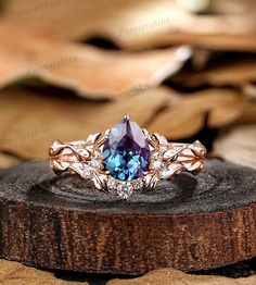 an engagement ring with a blue stone surrounded by leaves on top of a piece of wood