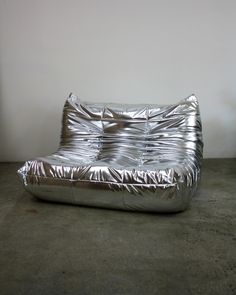 a shiny silver couch sitting on top of a cement floor