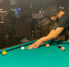 a man and woman leaning over a pool table with balls in front of them,