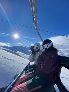 two skiers sitting on the side of a ski lift looking at the sun in the sky