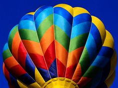 a multicolored hot air balloon is flying in the sky with blue skies behind it