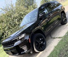 a black suv parked on the side of a road next to some grass and trees