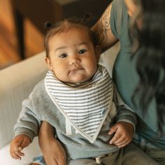 a woman holding a baby wearing a bib while sitting on top of a couch