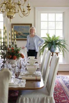 a woman standing in front of a dining room table with chairs and plates on it