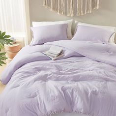 a bed with purple comforter and pillows in a room next to a potted plant