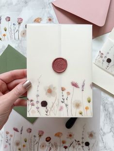 a hand holding a card with flowers on it and a wax stamp in the middle