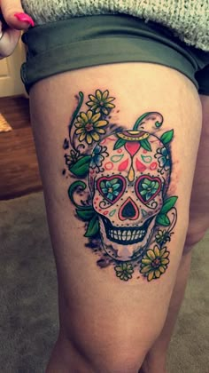 a woman's thigh with a skull and flowers tattoo on her leg, while she is wearing green shorts