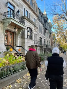 two people walking down the sidewalk in front of some buildings with pumpkins on them