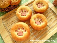 four dog paw shaped breads on a cooling rack with donuts in the background