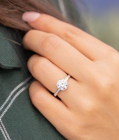 a woman's hand with a diamond ring on her left hand and a green sweater behind her