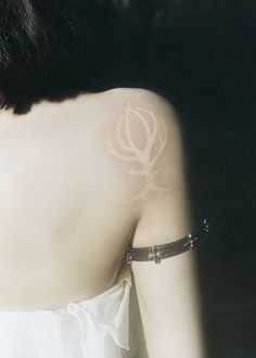 the back of a woman's shoulder with a white tattoo on her left arm