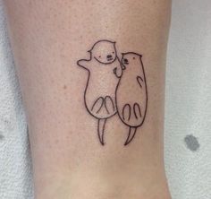 a small tattoo on the ankle of a woman with two otters hugging each other