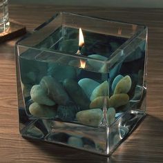 a candle that is sitting inside of a glass container filled with rocks and pebbles on a table