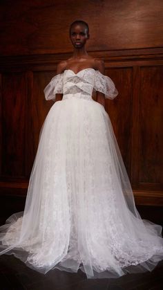 a woman in a white wedding dress standing next to a wooden paneled wall and wearing an off the shoulder veil