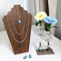 three necklaces are on display next to a vase with daisies and flowers in it