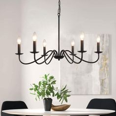 a chandelier hanging over a dining room table with chairs and a potted plant