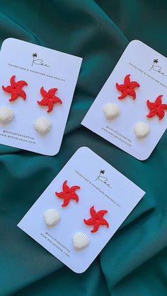 three red and white sea shells are sitting on a green cloth, one is in the shape of a starfish