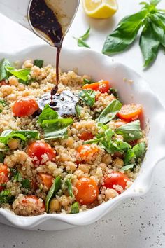 a white bowl filled with quinoa salad and dressing being drizzled over it